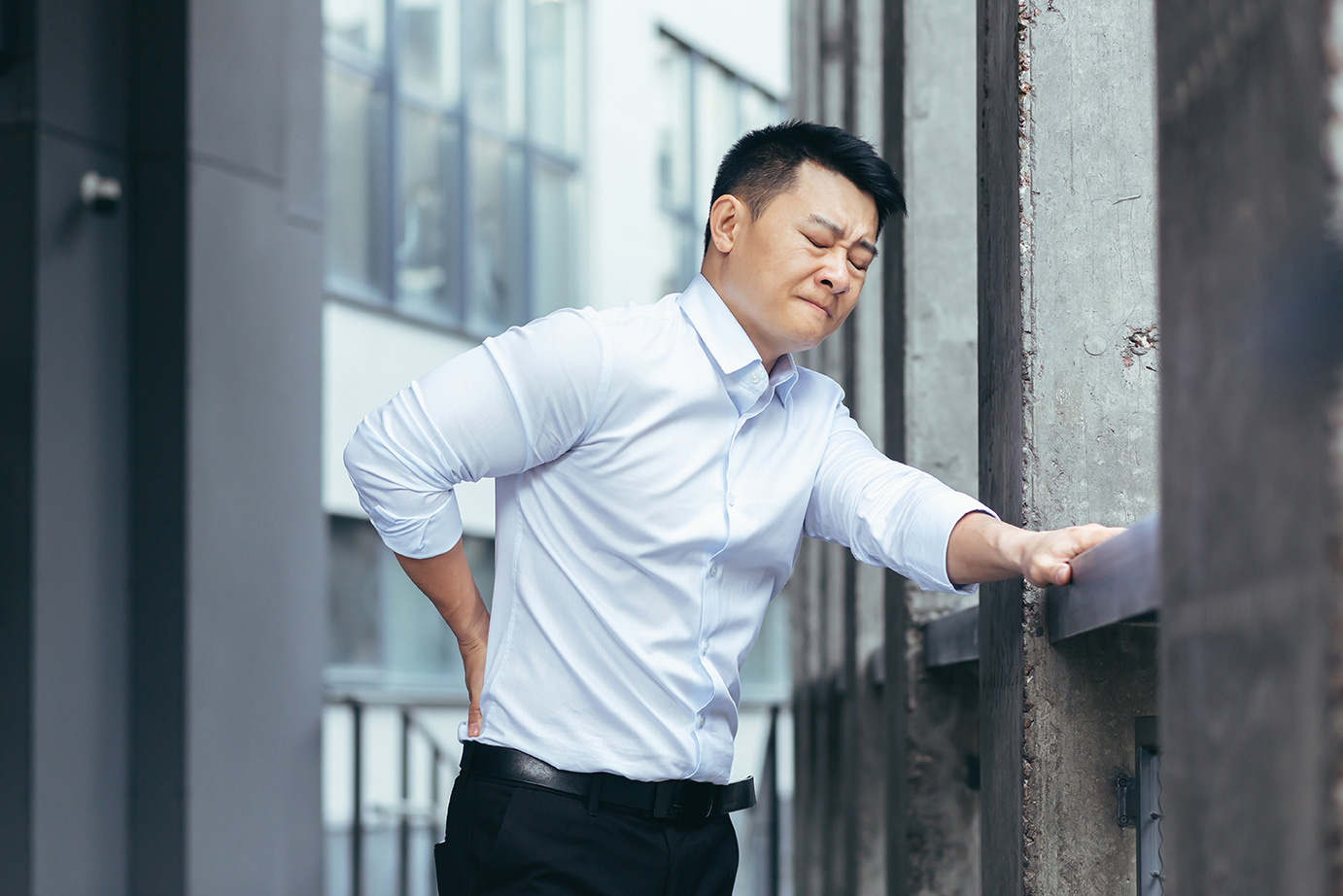 Man experiencing lower back pain and holding his back while standing. 