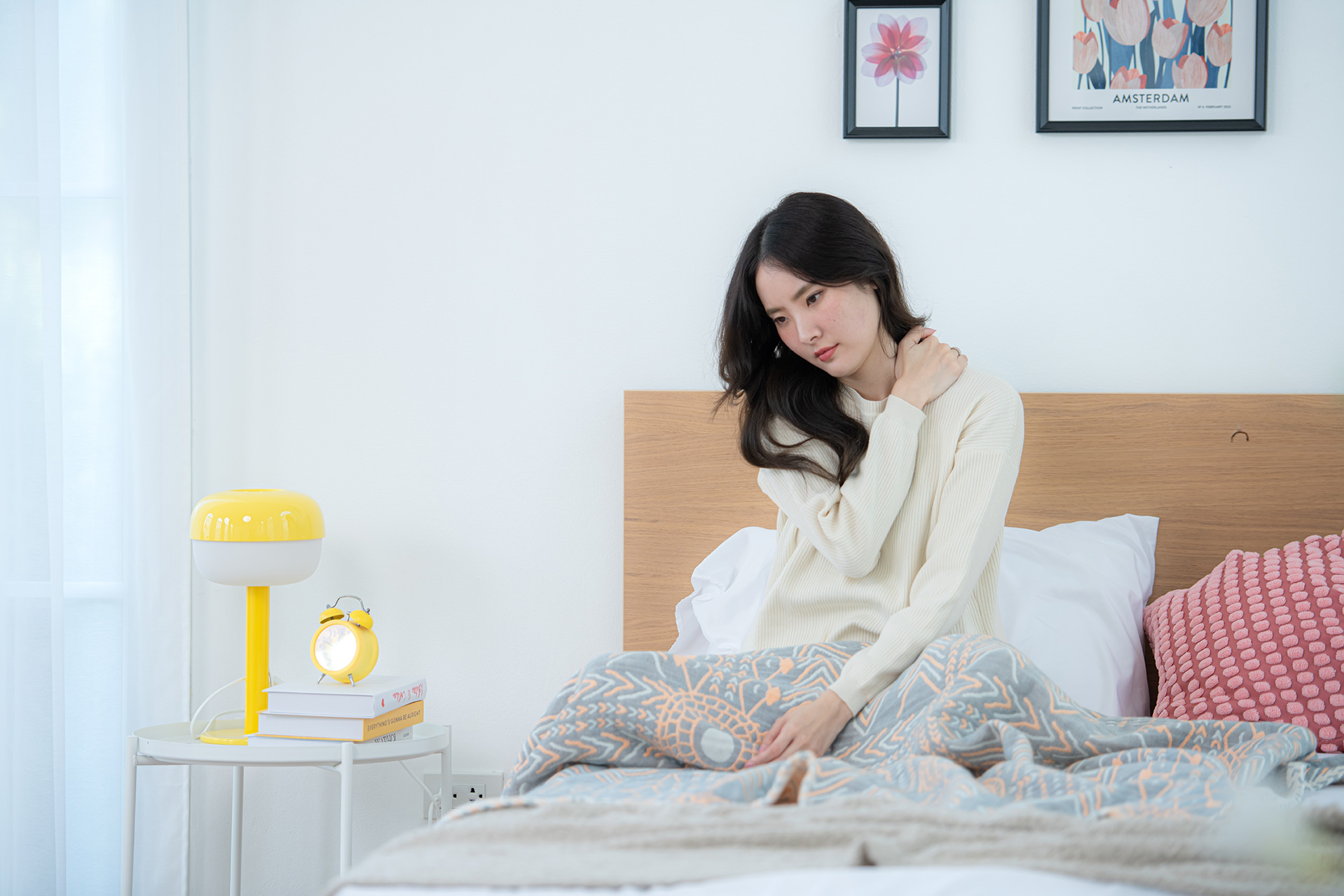 Woman sitting in bed, experiencing body aches and stiffness. 