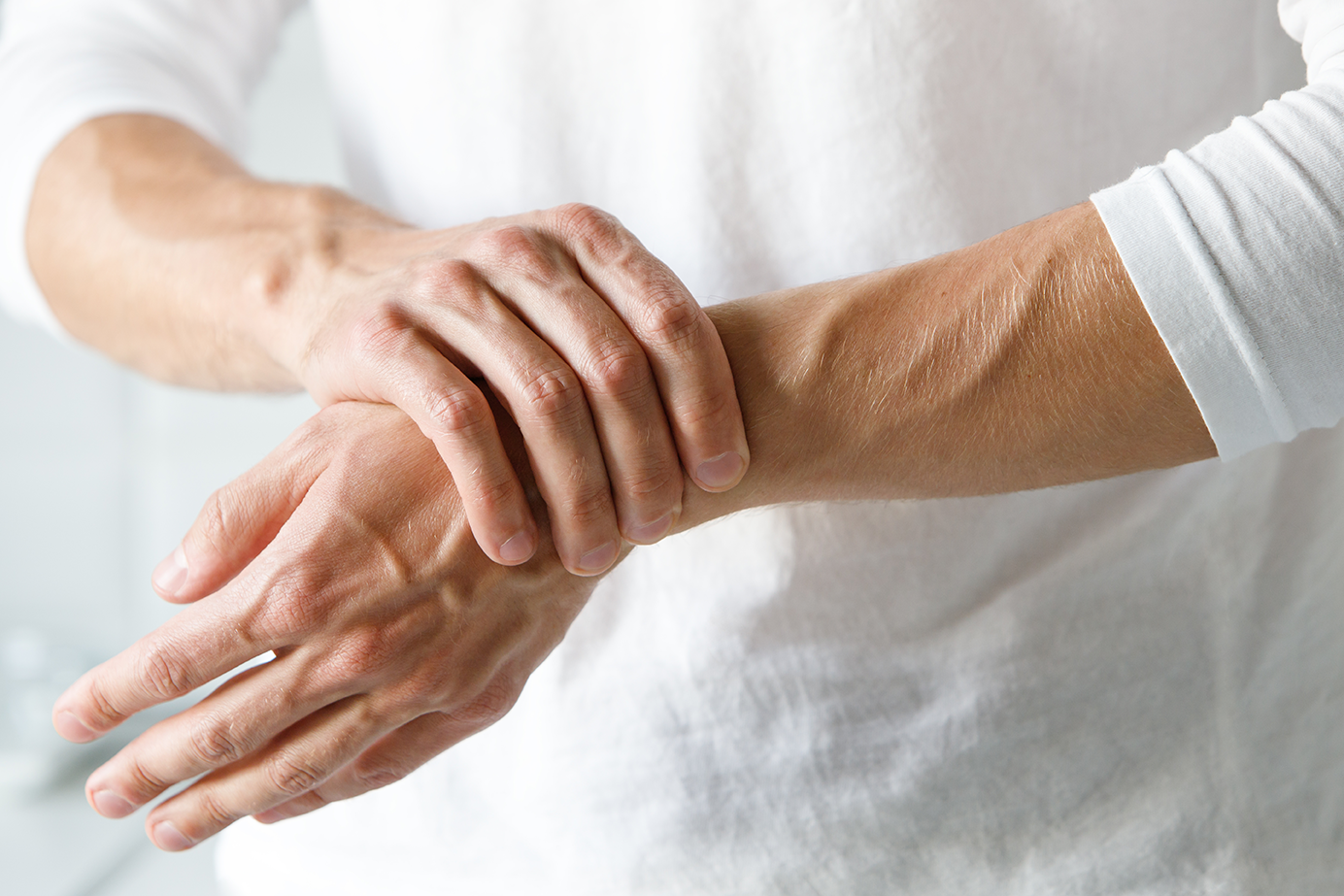 Close‑up of a man’s forearms and hands as he holds and supports his painful wrist, symbolising joint pain and stiffness experienced in rheumatoid arthritis.