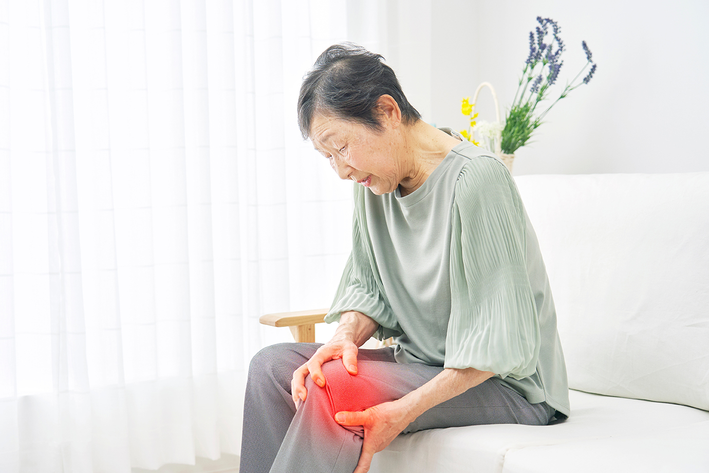 Elderly woman seated while holding her knee in discomfort, showing signs of persistent joint pain associated with rheumatoid arthritis.
