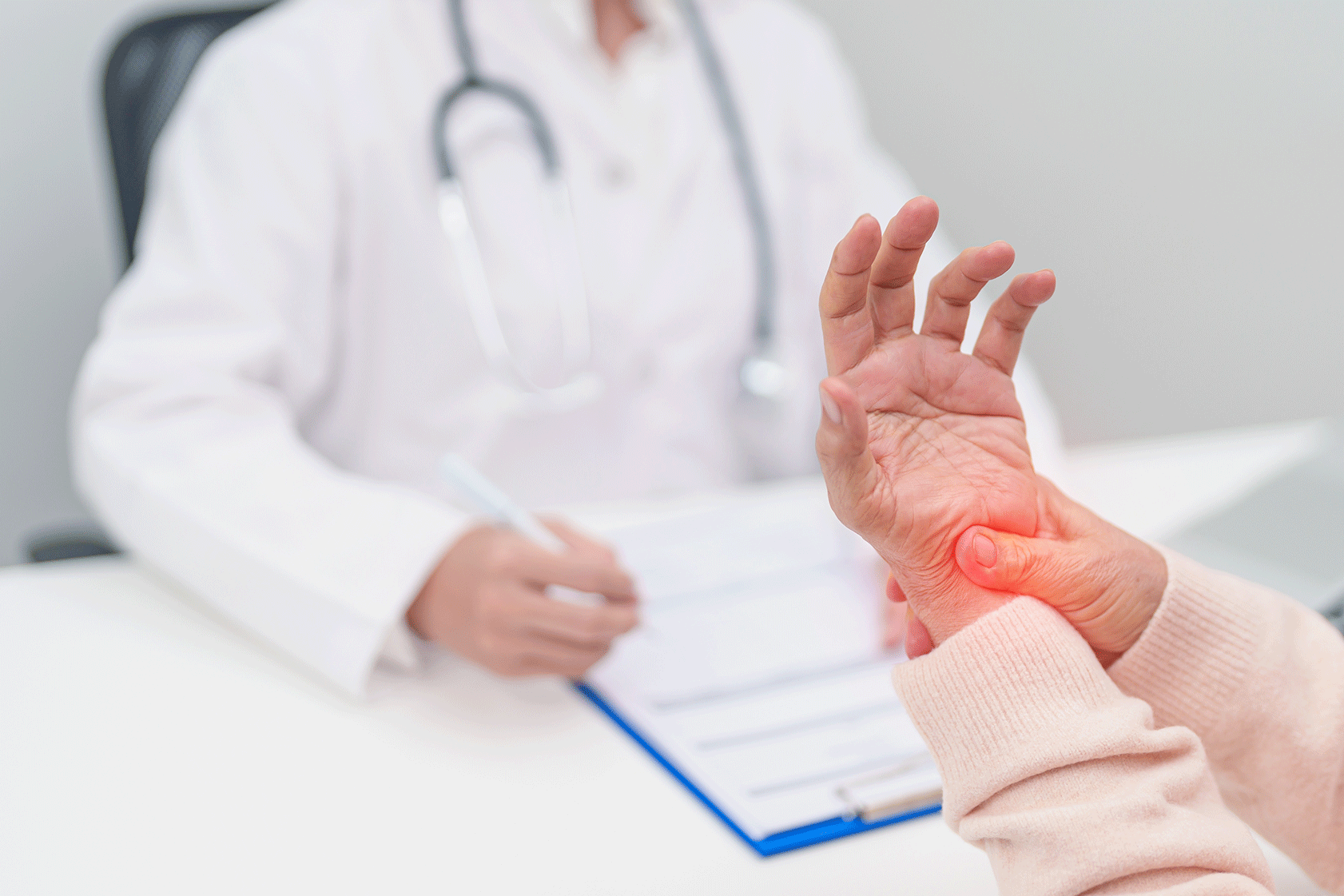 Elderly woman consulting a doctor while holding her wrist in pain, illustrating joint inflammation.