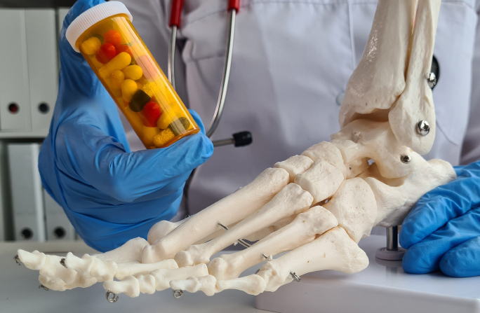 Rheumatologist holding medication for psoriatic arthritis and a skeletal model of a foot