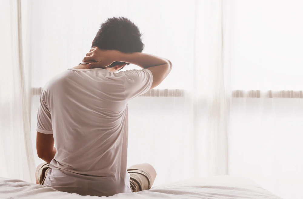 Man sitting on the edge of his bed and experiencing morning stiffness.