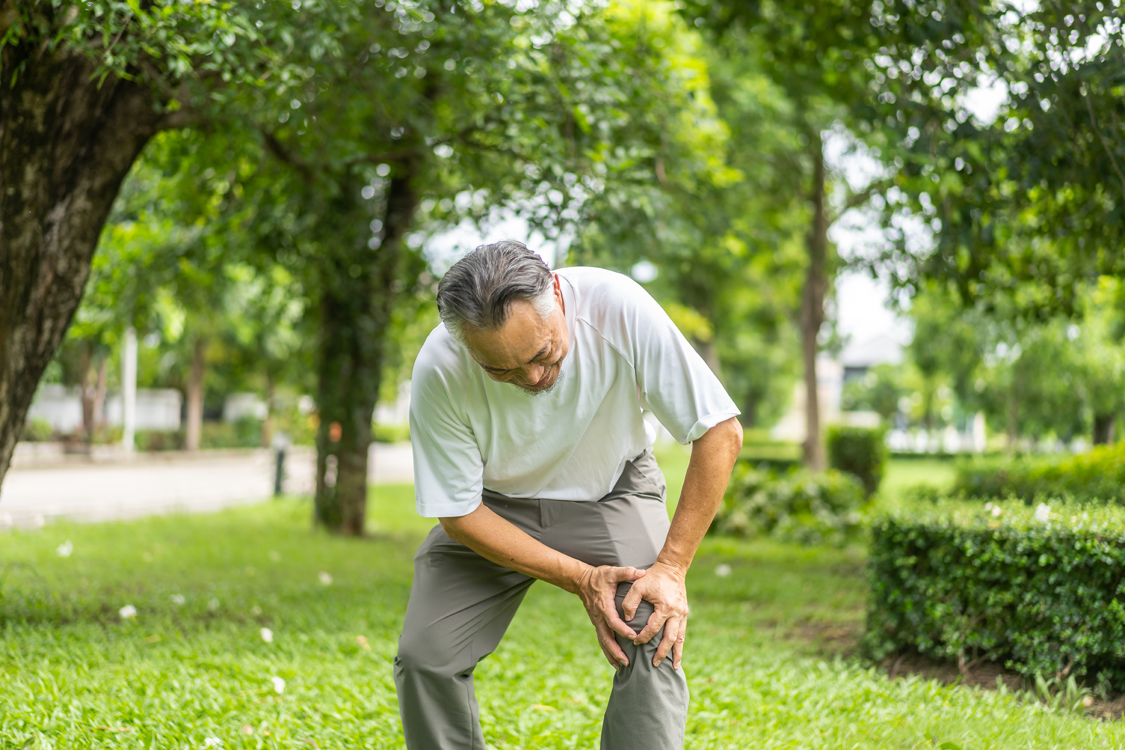 Elderly man holding his knee and showing signs of joint pain and stiffness.