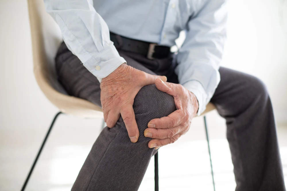 Man experiencing gout pain in his knee and holding the affected joint while seated.